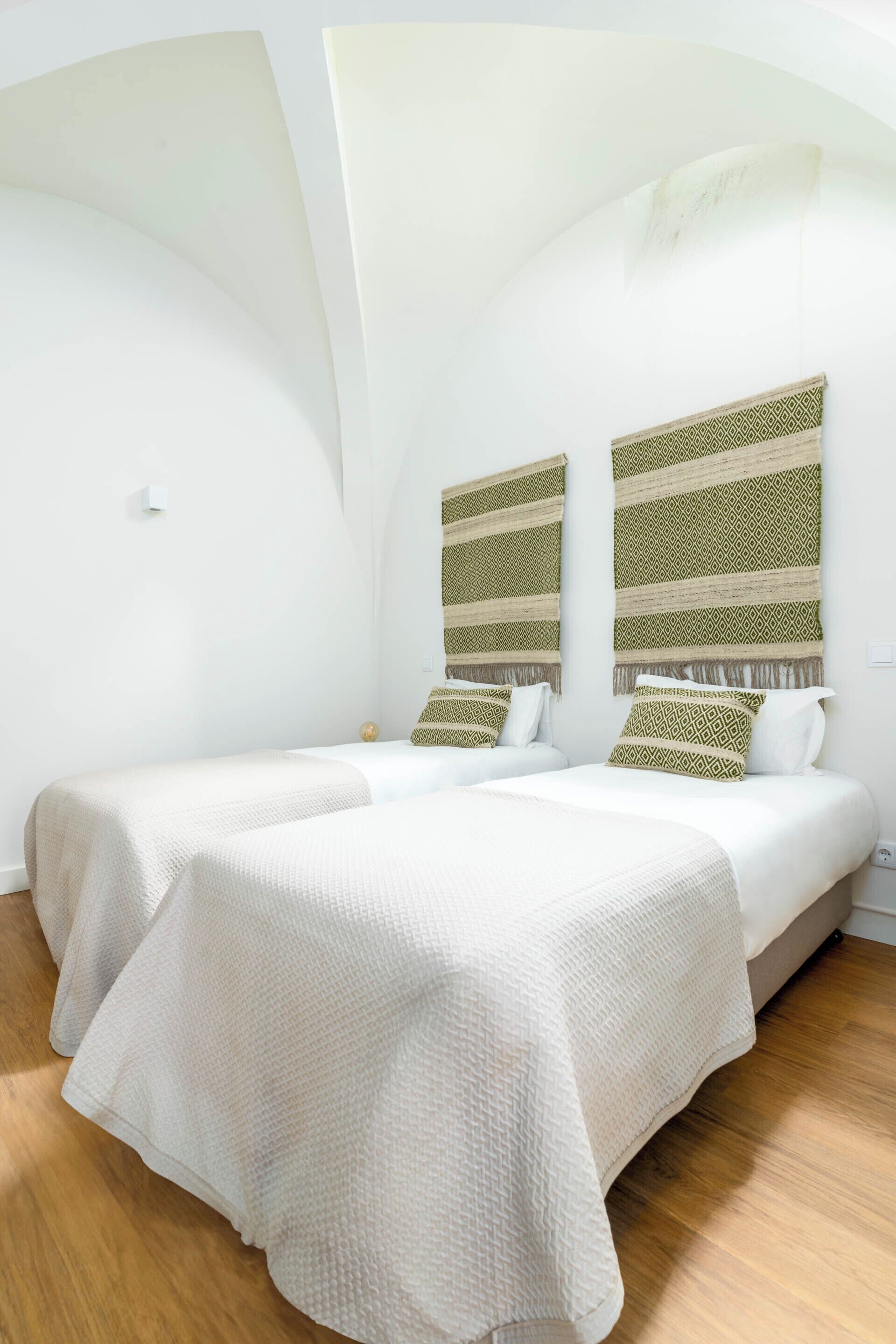 Quarto de hotel com duas camas, roupa de cama branca e cabeceiras estampadas.