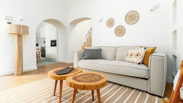 A modern living room with a sofa, two wooden side tables, a lamp, and a kitchen in the background.