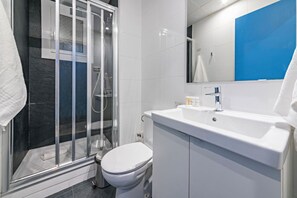 Et moderne badeværelse med en brusekabine med glasdør, et hvidt toilet og en vask med spejl over.