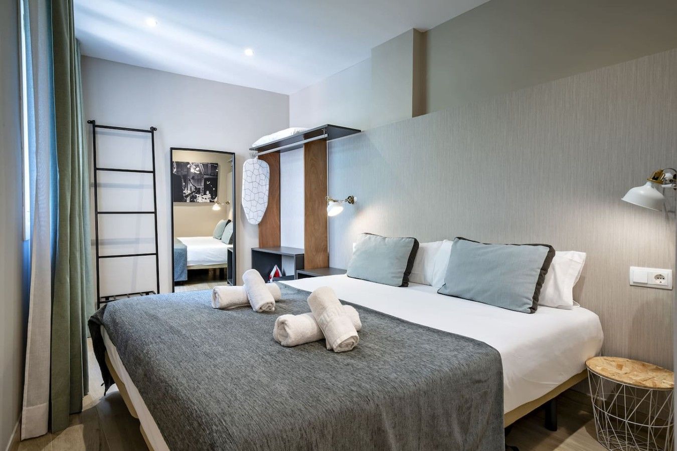 A modern hotel room with a large bed, a bedside table, a mirror, and a view of the room's interior.