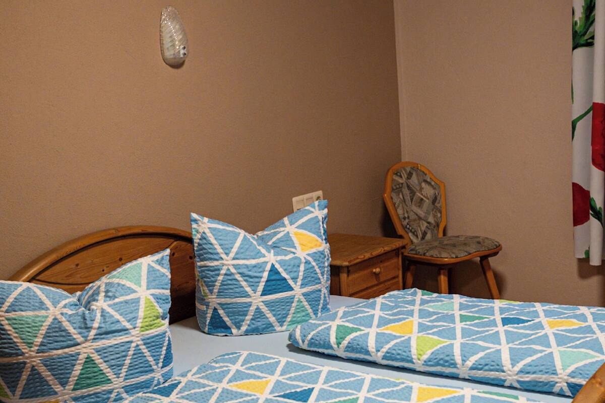 A wooden bed with a geometric patterned bedspread and pillows, a wooden nightstand, and a chair with a patterned cushion.