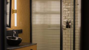Un baño moderno con un lavabo negro, un armario de madera, una cabina de ducha de vidrio y una pared de azulejos.