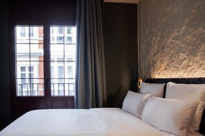 A hotel room with a large bed, a window with curtains, and a textured wall.