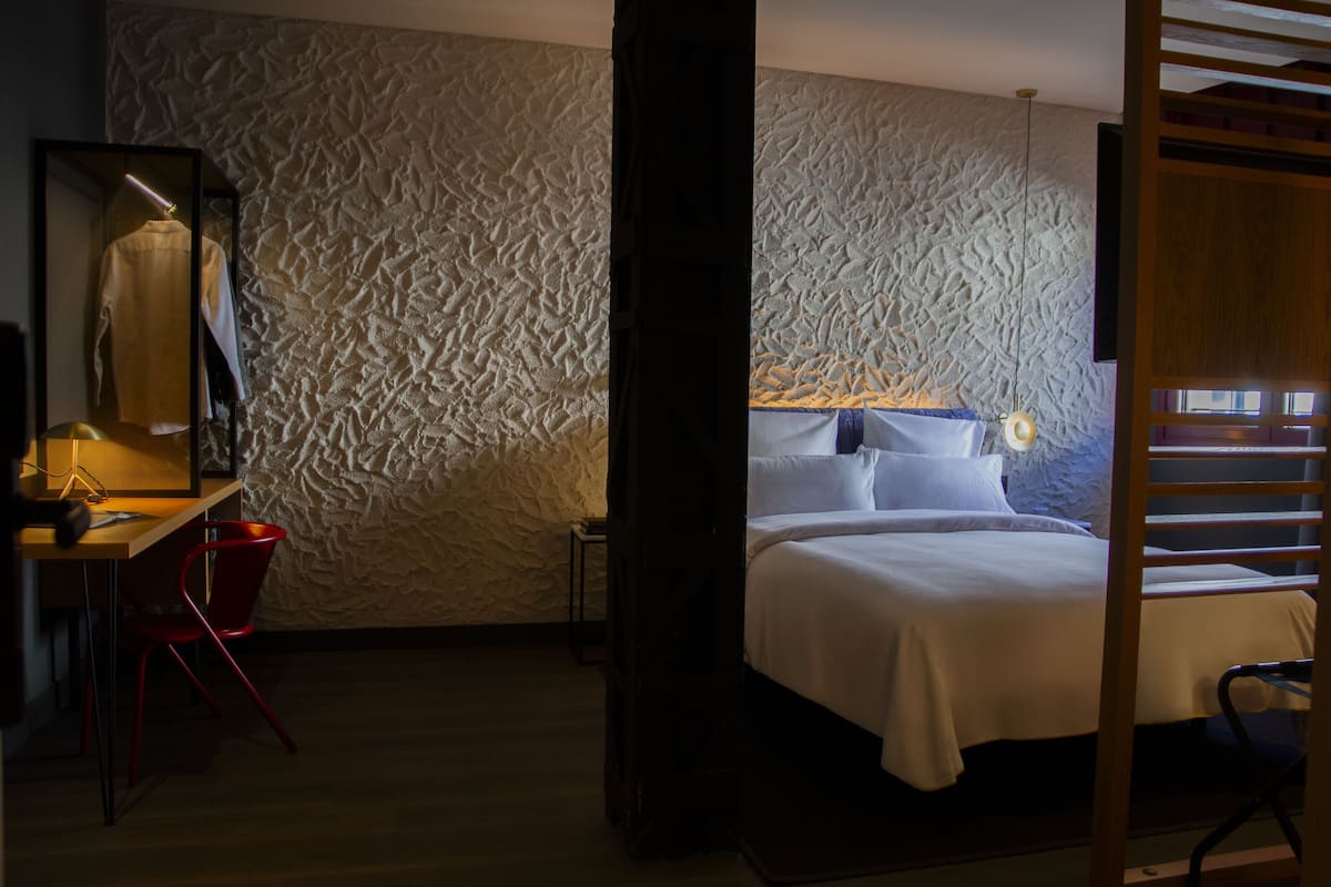 A bedroom with a textured wall, a bed with white linens, a desk with a chair, and a mirror.