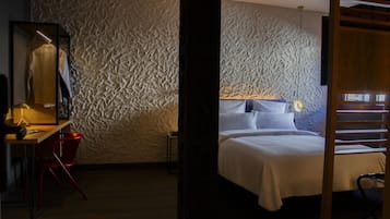 Un dormitorio con pared texturizada, cama con ropa de cama blanca, escritorio con silla y espejo.