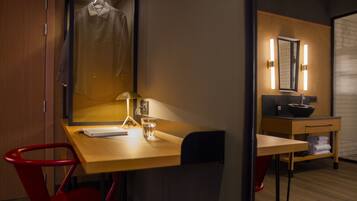 Habitación de hotel con un escritorio de madera, una silla roja, un espejo, un lavamanos y un perchero para toallas.