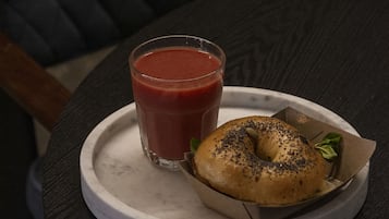 Una mesa con un vaso de bebida roja y un bagel sobre un plato blanco.