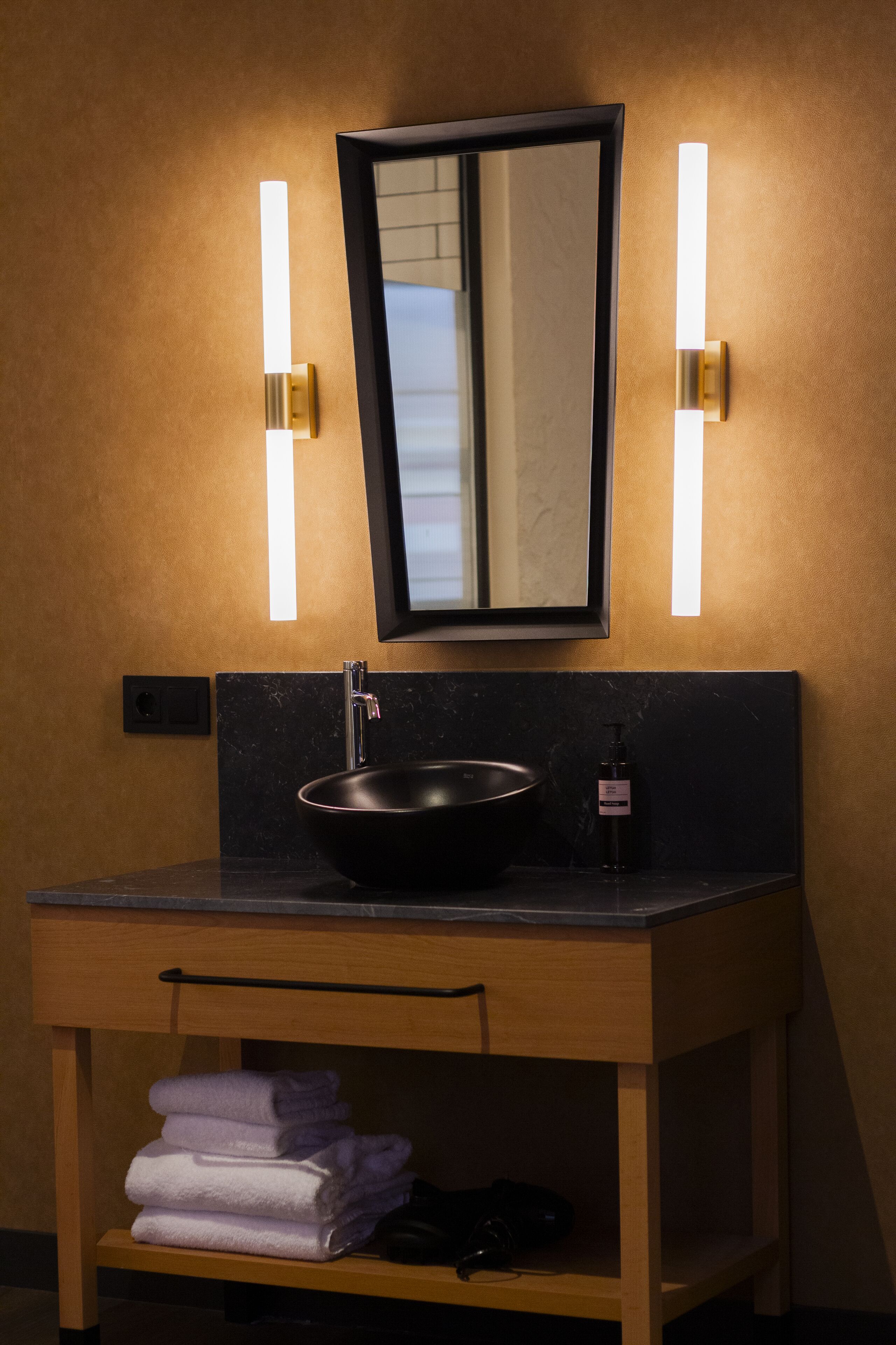 Une salle de bain avec un lavabo noir, un miroir et deux appliques murales.
