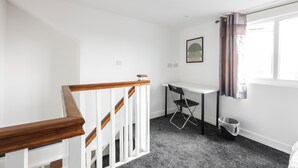 A room with a white staircase, a desk, a chair, a framed picture on the wall, and a window with curtains. - Cosy Apartment Near Leeds City Centre (Leeds)