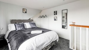 A modern bedroom with a large bed, a wooden bedside table, and a built-in wardrobe. - Cosy Apartment Near Leeds City Centre (Leeds)
