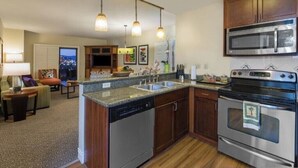Een moderne keuken met een vaatwasser, oven en magnetron. Er is een eethoek met een tafel en stoelen, en een uitzicht op de stad 's nachts.