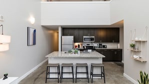 A modern kitchen with dark cabinets, a central island with stools, and a microwave. - Modern Oasis: 2-Story Loft, 2bd/2bth Downtown (Des Moines)