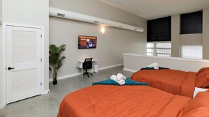 A hotel room with two beds, a desk, a chair, a potted plant, and a TV on the wall. - Modern Oasis: 2-Story Loft, 2bd/2bth Downtown (Des Moines)