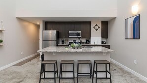 A modern kitchen with a central island, stainless steel appliances, and bar stools. - City Haven: Modern Loft 2bd/2bth Downtown DSM (Des Moines)