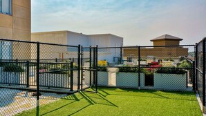 A fenced outdoor area with artificial grass, a chain-link fence, and buildings in the background. - City Haven: Modern Loft 2bd/2bth Downtown DSM (Des Moines)