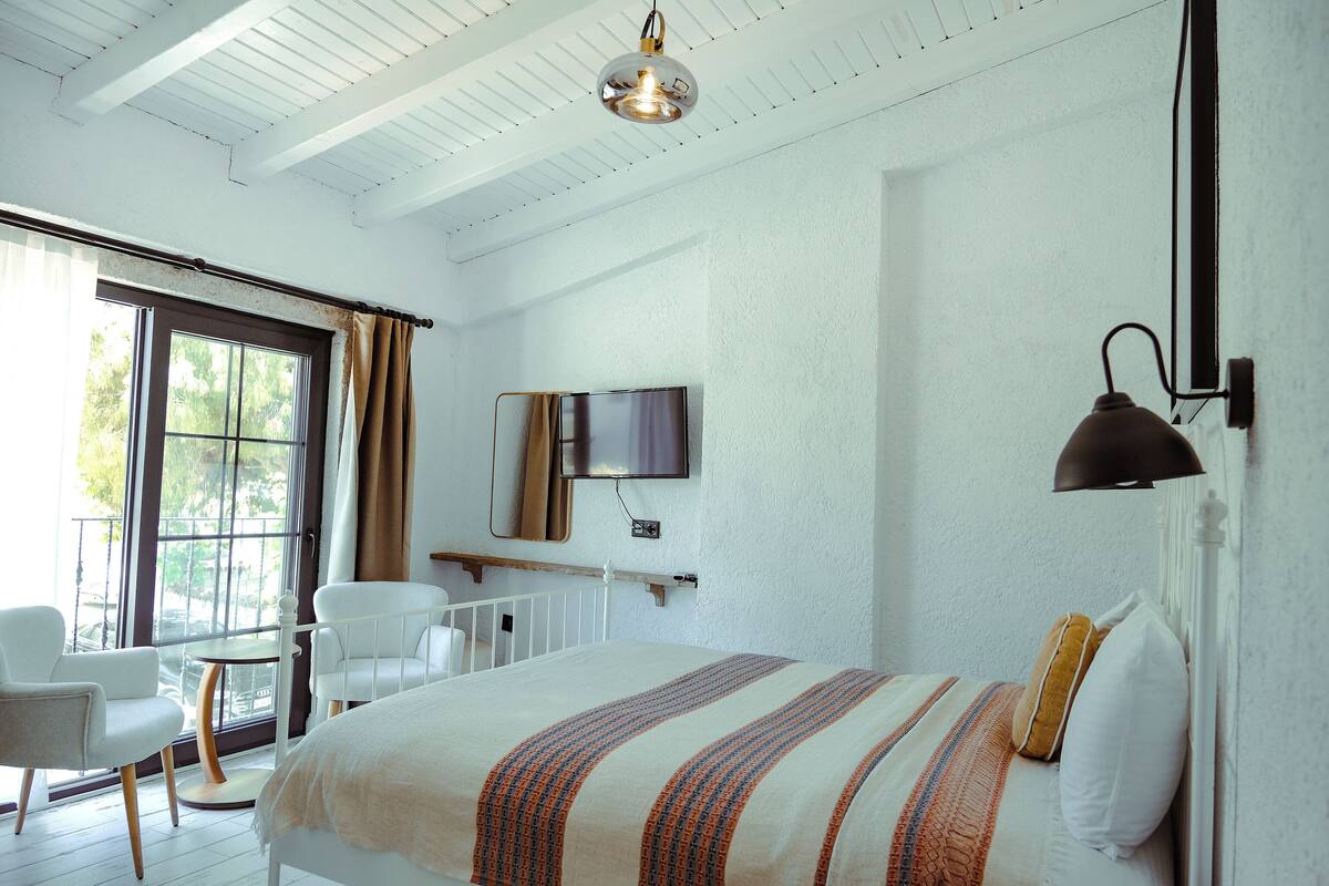 A bedroom with a bed, a television, a chair, and a window with curtains.