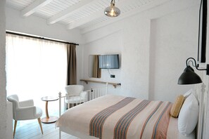 A bedroom with a bed, a TV mounted on the wall, a chair, and a small table. - Piraye Alaçatı (Cesme)