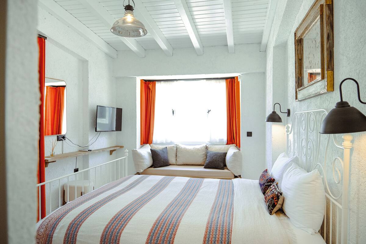 A bedroom with a bed, a television, and a window with curtains.