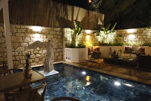 A pool area with stone walls, a statue, and seating. - Piraye Alaçatı (Cesme)