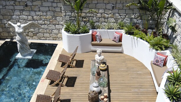 Area piscina con una statua, poltroncine da relax, un pontile in legno e fioriere con piante.