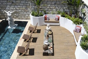 A poolside area with a statue, lounge chairs, a wooden deck, and planters with greenery. - Piraye Alaçatı (Cesme)