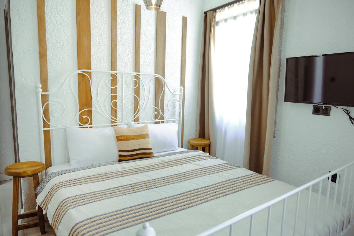 A neatly made bed with a striped bedspread, a white metal headboard, and a television mounted on the wall.