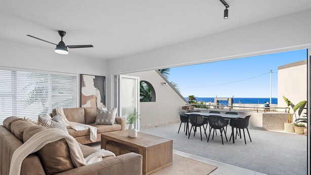 A modern living room with a sofa, coffee table, and dining area with chairs. There is a ceiling fan, a large window with blinds, and a view of the ocean. - Perna Perna Coastal Escape (Durban)
