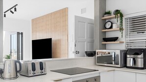 A modern kitchen with a flat-screen TV, a toaster, a kettle, a microwave, and a coffee maker. - Perna Perna Coastal Escape (Durban)
