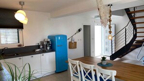Eine kompakte Küche mit blauem Kühlschrank, einem Esstisch mit Stühlen, einer Pendelleuchte und einer Treppe.