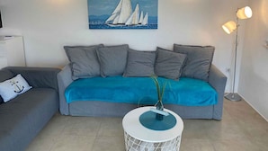 Ein Wohnzimmer mit grauem Sofa, einer blauen Decke, einem runden Couchtisch mit Pflanze und einem Segelboot-Gemälde an der Wand.