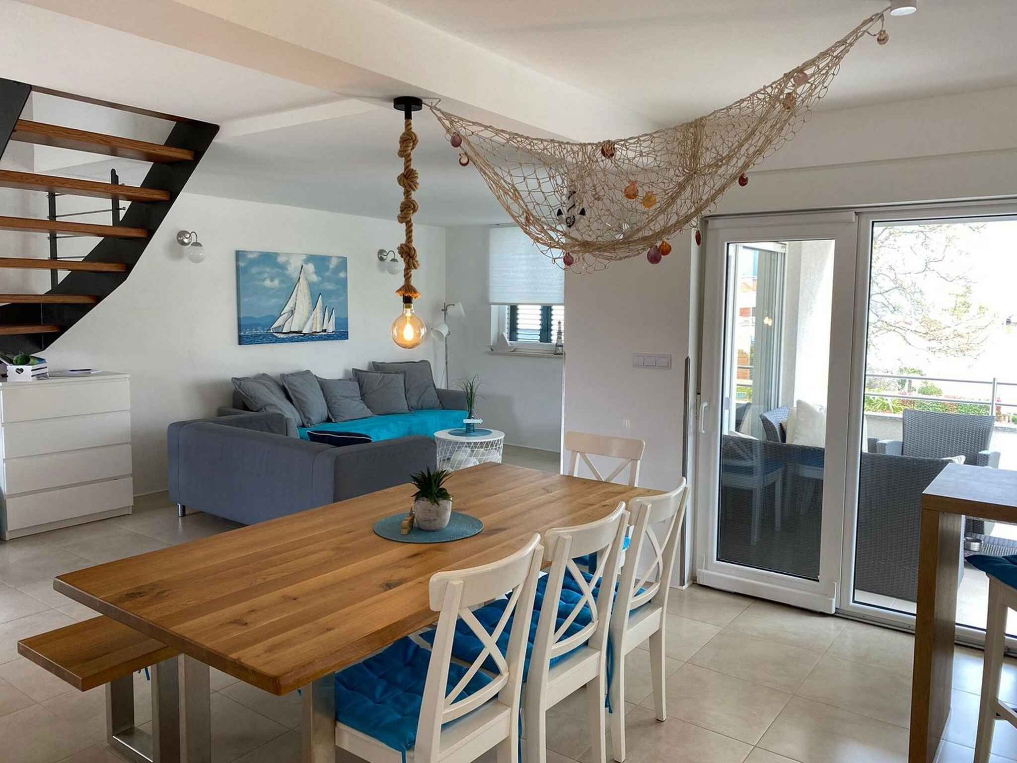 A modern kitchen with a wooden dining table, white chairs, and a hanging light fixture.