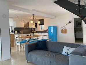 A modern kitchen with a dining area, a blue refrigerator, and a gray sofa with a pillow.