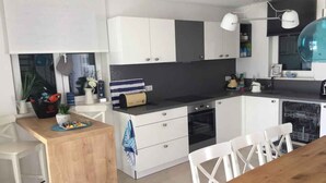 Eine moderne Küche mit weißen und grauen Schränken, einer Holztischinsel, weißen Stühlen und einem Esstisch aus Holz.
