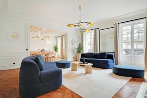 A modern living room with a blue sofa, ottomans, a coffee table, and a chandelier. - LUXURIOUS 4-BEDROOM PARISIAN RETREAT: PALAIS-ROYAL GEM 4 UNFORGETTABLE GETAWAYS! (Paris)