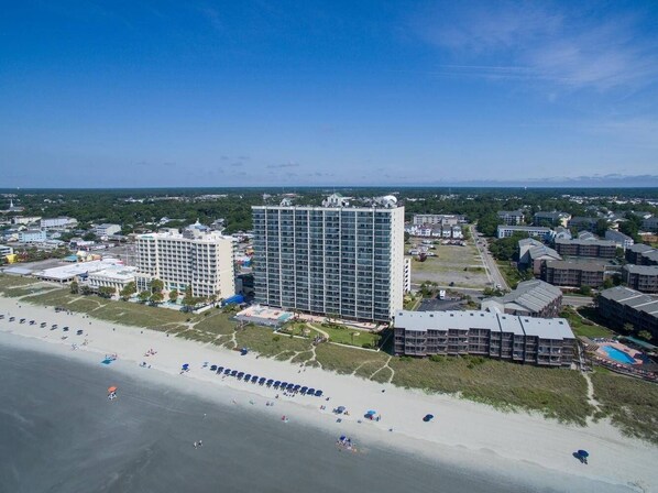 A coastal hotel with multiple buildings, a beach, and a clear sky.