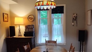 A dining room with a large wooden table, chairs, a chandelier, a bookshelf, and a window with curtains. - Quaint farmhouse with garden, big yard, river access- all near Middlebury, VT. (Weybridge)