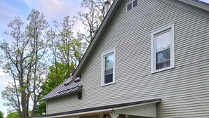 A two-story house with a covered porch, a chimney, and a lawn. - Quaint farmhouse with garden, big yard, river access- all near Middlebury, VT. (Weybridge)