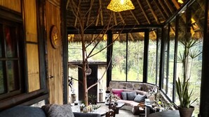 A cozy room with a blue sofa, a dining table, and a large window overlooking a lush garden. - Finca de la Vaca - Casa el Mirador (Cumandá)