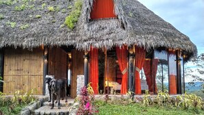 A thatched-roof building with a wooden door and a dog in front. - Finca de la Vaca - Casa el Mirador (Cumandá)
