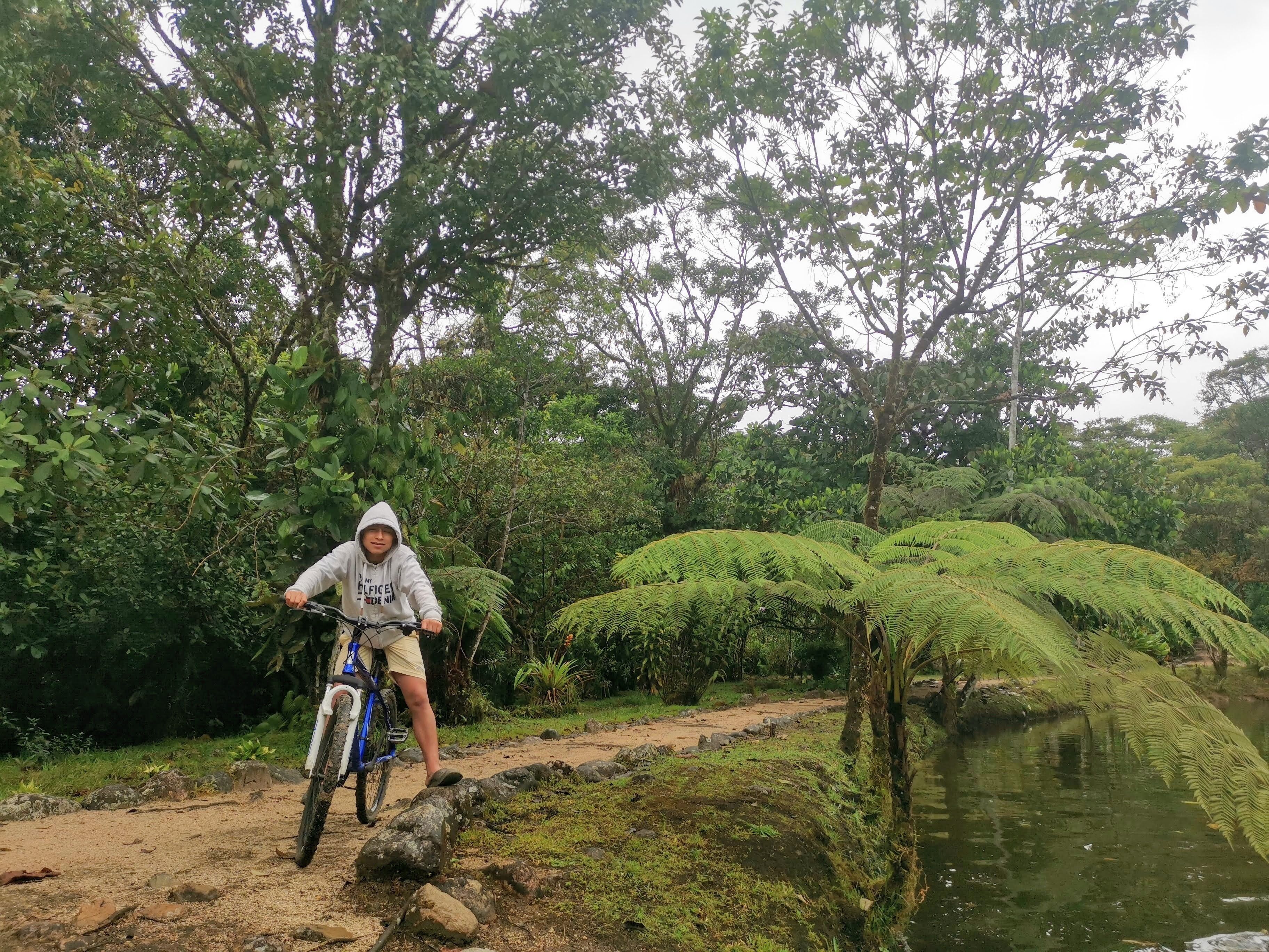 Una persona en bicicleta en un entorno natural, con abundante vegetación y un cuerpo de agua.