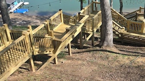 Une terrasse en bois avec un escalier menant à une zone de quai au bord d’un lac.