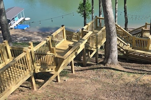 Une terrasse en bois avec un escalier menant à une zone de quai au bord d’un lac.