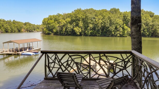 Une terrasse en bois avec deux bancs donnant sur un lac paisible, le tout entouré d’une forêt dense.