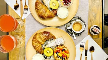 Taula de dinar amb dues platades d'esmorzar, incloent croissants, fruita i pastissos, juntament amb coberts i vasos de suc d'aranja.
