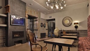 A modern living room with a fireplace, a television mounted on the wall, a chandelier, and a dining area with a table and chairs. - Forvm Bijoux ROOMS (Trieste)