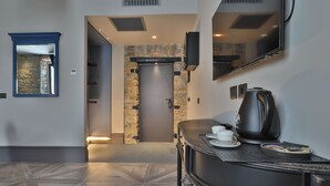 A modern hotel lobby with a stone wall, a flat-screen TV, a coffee station, and a patterned floor. - Forvm Bijoux ROOMS (Trieste)
