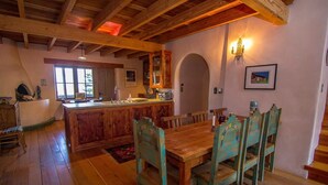 A rustic interior with a wooden dining table and chairs, a kitchen area with a bar, and a fireplace. - Caja de Tesoro ~ A Romantic Mountain Getaway! (Arroyo Seco)