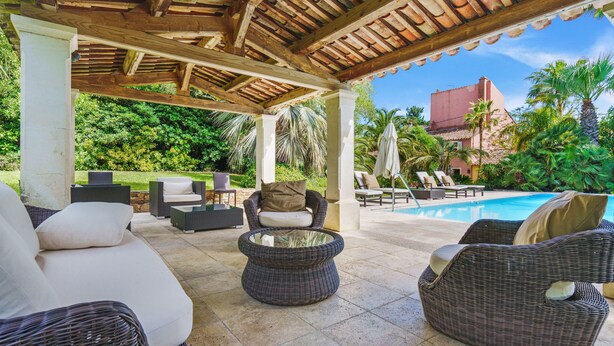 Un espace extérieur aménagé en terrasse, avec des meubles en osier, une piscine et une végétation luxuriante.