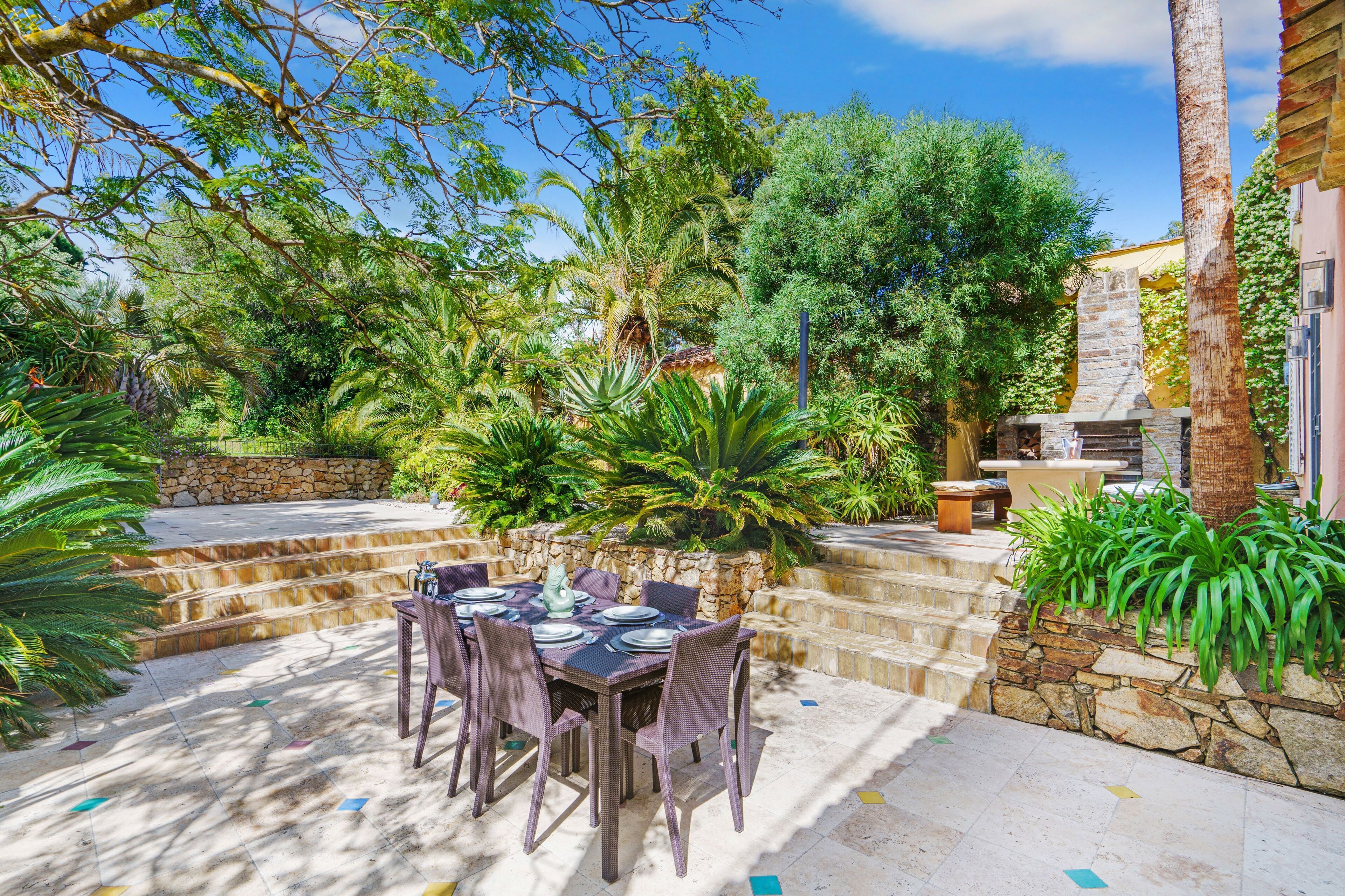 An outdoor dining area with a stone wall, a stone staircase, and lush greenery.