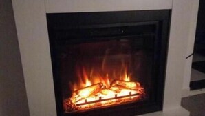 A modern fireplace with a clean, white surround and a glass front, providing a clear view of the fire. - Guesthouse Jazmines Mozàrabes (Baena)